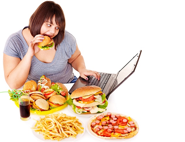Женщина кушает вредную пищу и смотрит в ноутбук