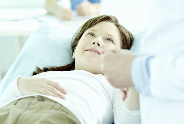 Девочка лежит на кушетке в больнице и держит за руку доктора