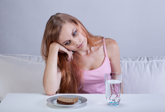 Девушка сидит за столом со стаканом водой и кусочком хлеба в тарелке
