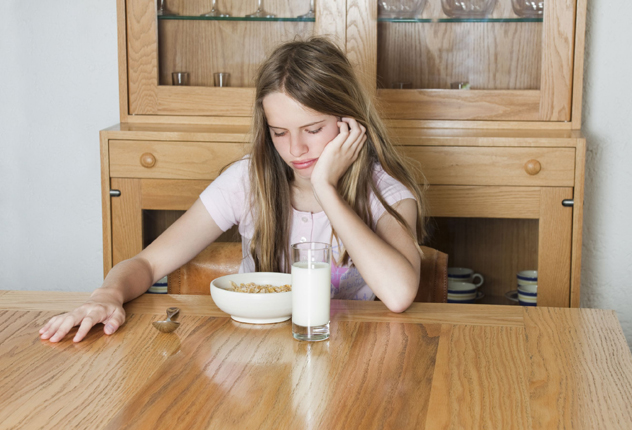 Девушка сидит за столом и не хочет есть кашу с молоком