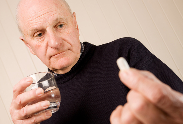 Пожилой мужчина держит в руках таблетку и стакан с водой