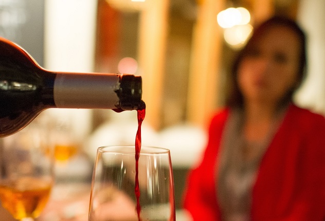 Женщина смотрит как в стакан наливают вино