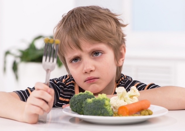 Мальчик сидит за столом и не хочет кушать овощи