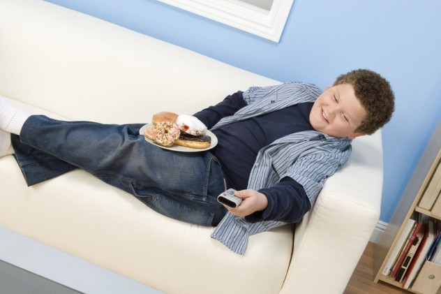 мальчик сидит на диване с пультом и сладостями