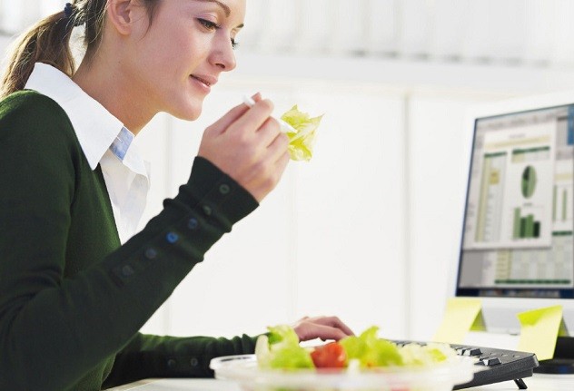Женщина кушает салат перед компьютером